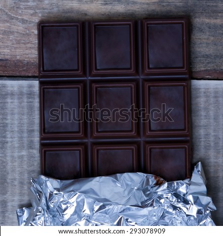 Open the foil-wrapped chocolate bar lying on a wooden surface.close-up.plan view