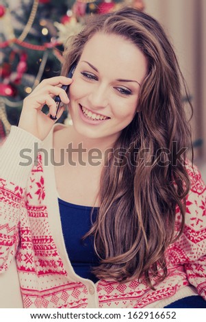 Happy young woman near Christmas tree making phone call