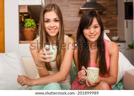 Two happy young female friends with coffee cups enjoying a conversation in the living room at home