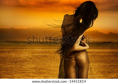 Sexy model with hair blowing in wind and sunset ocean in background