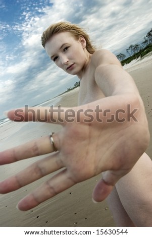 stock photo Blonde girl naked on beach holds up hand to camera