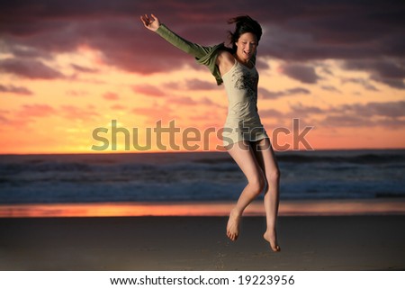Happy girl jumps for joy on beach with sunrise in background