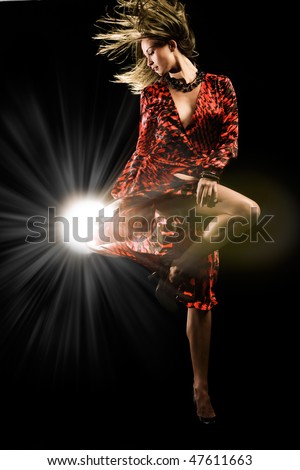 Beautiful girl in red dress dances on black studio background