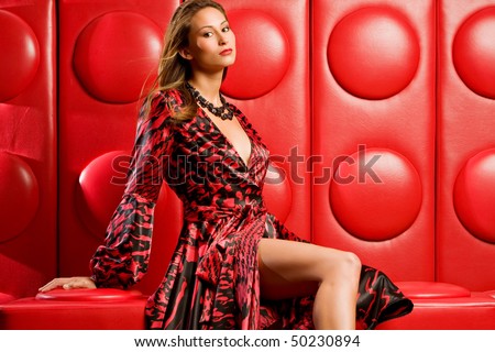 Beautiful fashion model sits on funky modern red lounge
