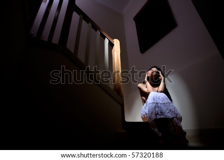Beautiful girl sits alone on stairs in dark house
