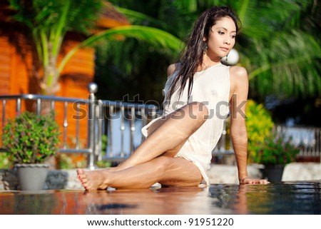 Sexy Asian woman lays on edge of pool in tropical resort in Thailand