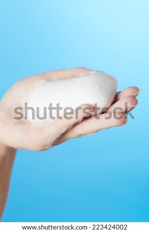 Woman\'s hand in foam of shower gel with soap on blue background