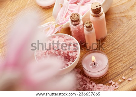 Spa still life with pink sea salt and flower petals on wooden background