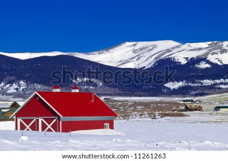A classic red barn in Colorado winter with snow capped mountain peaks, portrays rural America