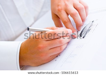 Closeup of a business man holding a pen in one hand and pointing with the other hand analyzing pie chart and making notes