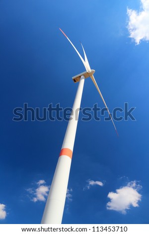 Wind power station wind turbine against clear blue sky and small clouds
