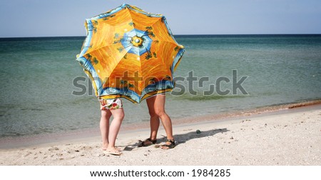 Two ladies hiding behind a big beach umbrella