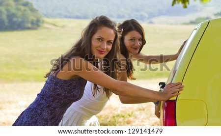 two girls pushing a yellow car in the  fields