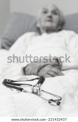 elderly woman lying ill in her bed with a stehoscope , black and white