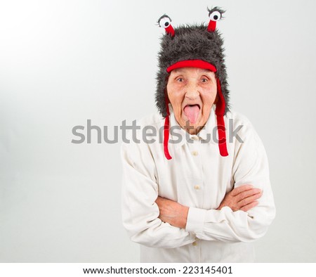 very old lady in funny fur hat with two tentacles puts her tongue out