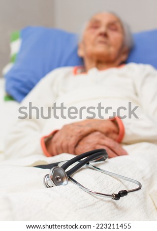 elderly woman lying ill in her bed with a stehoscope , black and white