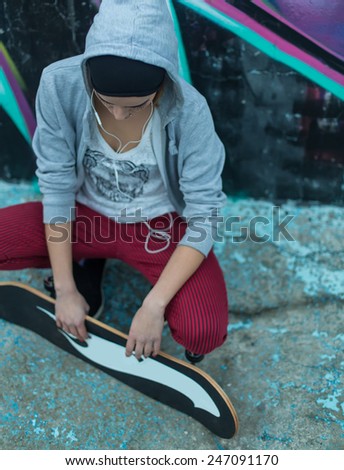 Street girl holding her skateboard next to a graffiti wall.
