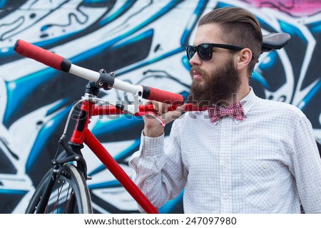 Young hipster man with a bike posing near a wall full of graffiti.