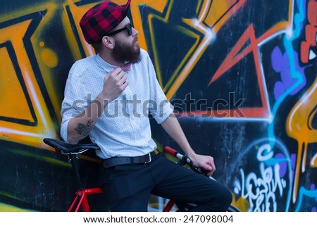 Young hipster man with a bike posing near a wall full of graffiti.
