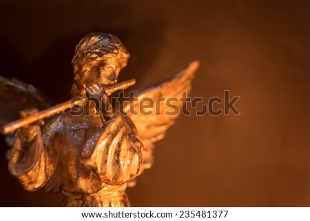 Winged angel playing the flute in warm light and gold tones.