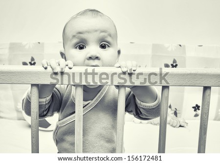 Sad baby girl in her crib, black and white image