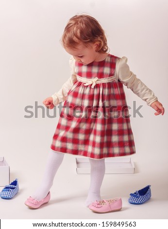Pretty little girl sitting on the floor, taking on pink shoes