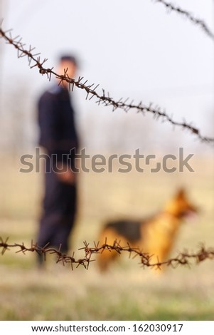 Silhouette of a soldier and wolf dog behind a barbed wire fence