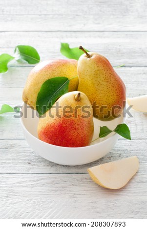 Ripe pears with leaves in white bowl over white wood table