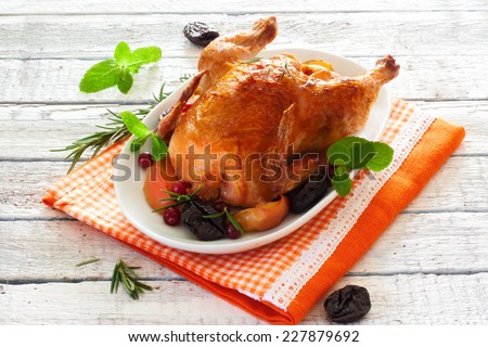 Roasted whole chicken with prunes and apples over white wood background