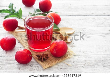 Glass of plum juice and ripe plums over white wood background