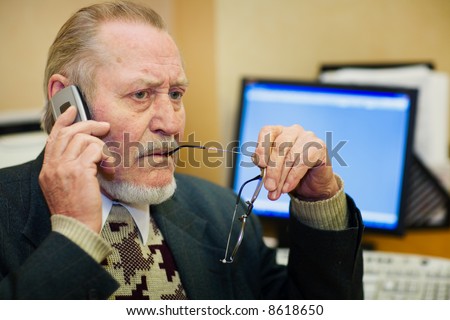 Mature businessman talking on the phone, checking out a document on his computer monitor.