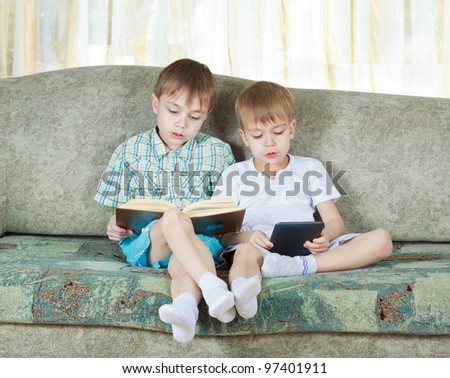 Two reading boys at sofa. One with paper book, other with electronic book