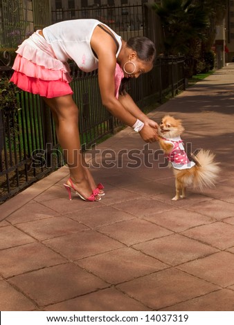 Attractive African-American young woman dancing with smiling small Pomeranian Spitz dog, that walks on rear legs, pink, skirt