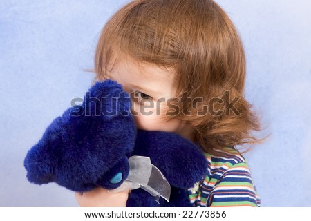 peekaboo - shy kid holding blue Teddy bear and peeking from behind blue stuffed animal toy (blue background)