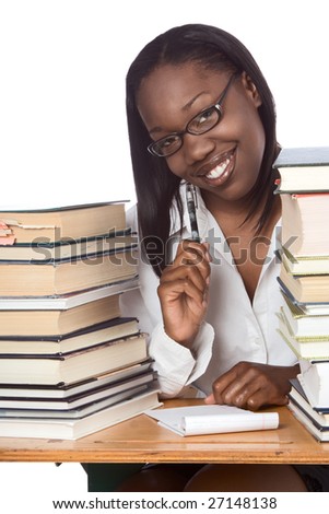 African-American ethnic black young female student in eyeglasses with pen and notepad sitting at school desk by piles of books