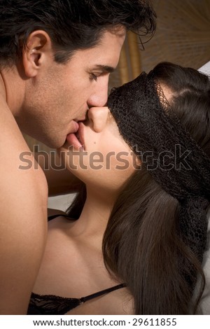 Loving affectionate heterosexual couple in affectionate sensual kiss. Woman eyes are covered by black scarf. Mid adult Caucasian men in late 30s and young Hispanic woman in early 20s