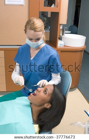 Young African-American ethnic black female opening her mouth while blond Caucasian dentist in white latex gloves and mask check condition of her teeth