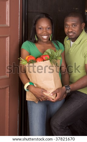 Young ethnic African American couple coming back home, returning from store with paper bag full of vegetables