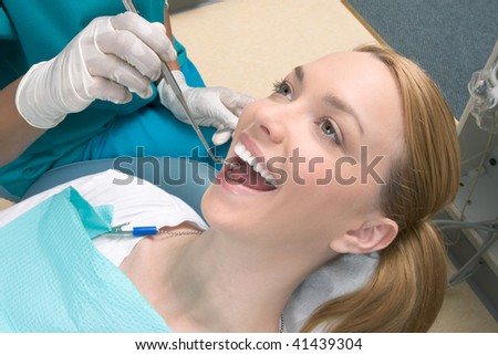 Young blond Caucasian female opening her mouth while African-American ethnic dentist in white latex gloves check condition of her teeth