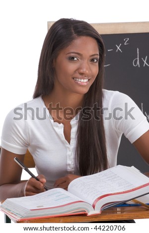 High school or college ethnic African-American female student sitting by the desk at math class. Blackboard with advanced mathematical formals is visible in background