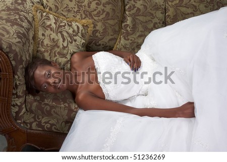 African American happy female in white gorgeous wedding gown lying down on couch