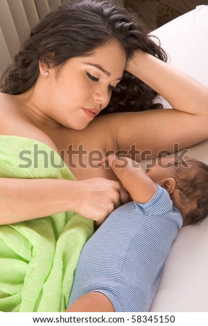 stock photo Latina woman lying on bed and breastfeeding her 2 months old