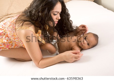 Hispanic mom lying down on bed and holding her biracial mix of Hispanic and African American infant son (baby is 7 weeks old)