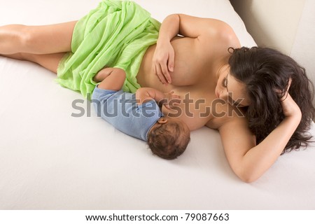 Latina woman lying on bed and breastfeeding her 2 months old baby of mixed Hispanic and African-American ethnicity