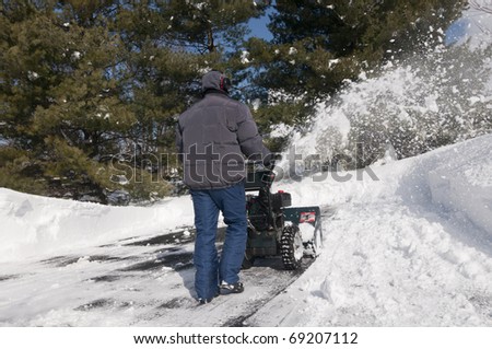 Man using snow blower to clear parking lot and driveway