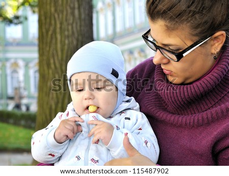 Baby sits on mother lap and eats corn ball