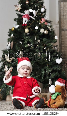 Baby in Santa costume sit near decorating Christmas tree with present toy