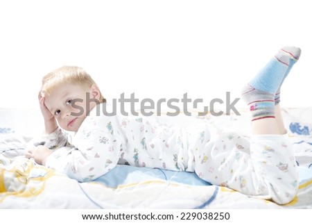 Funny cute little child in pajamas with blonde hair lies on a bed