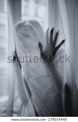 The young beautiful girl poses behind a curtain