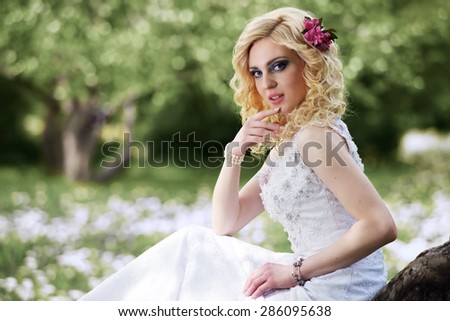 Beautiful young bride in white dress sits on tree in summer green park